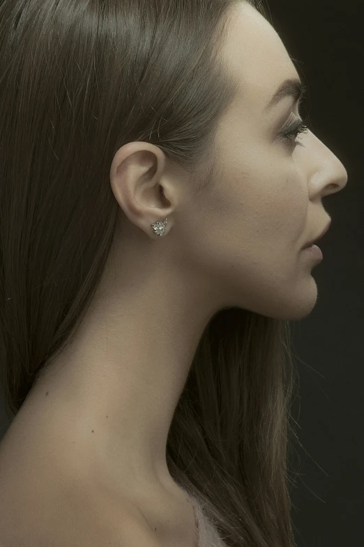 a woman with ear piercings wearing her hair up and looking off