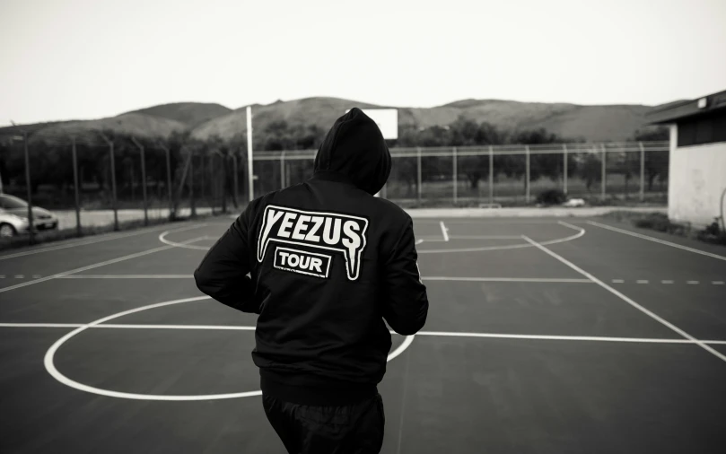 man in black hooded sweatshirt walks through an outdoor tennis court