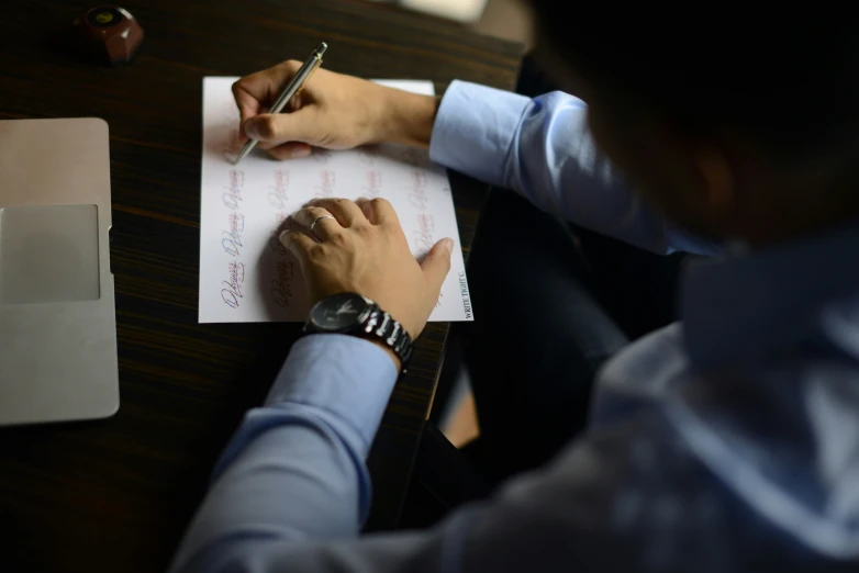 a man writing soing on paper while sitting at his desk