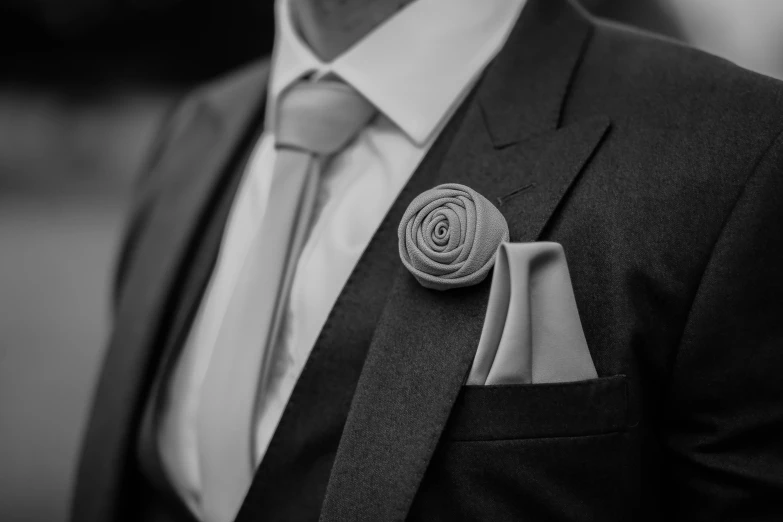 the man is wearing a gray tie and has a boutonniere with an ornate design on it