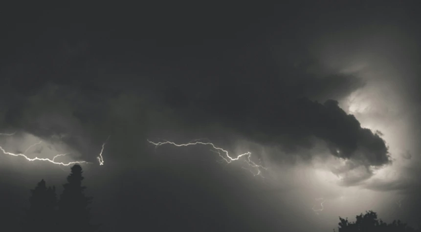 lightning coming from behind some clouds with trees in the foreground