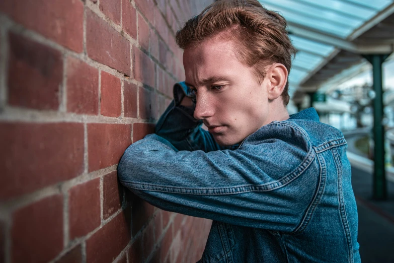 a young man leaning against a wall while holding onto a blue backpack