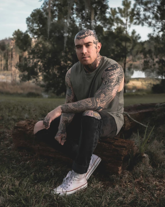 a man with tattooed arms sitting on a wooden log