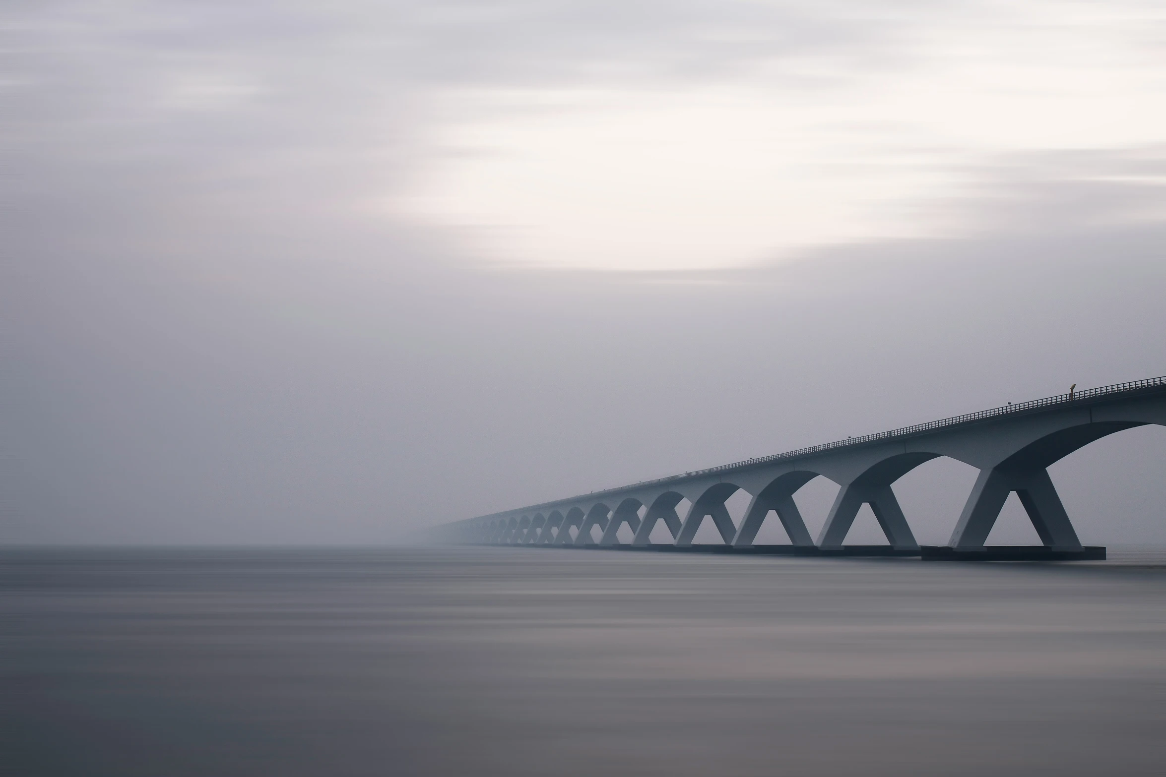 a gray bridge extending over water under a cloudy sky