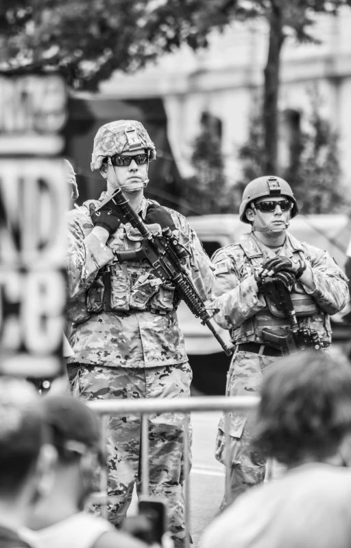 two soldiers stand with their guns while people watch