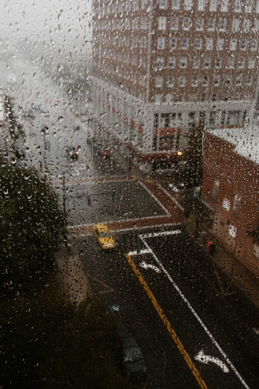 the view from inside a rainy window showing a street and a building