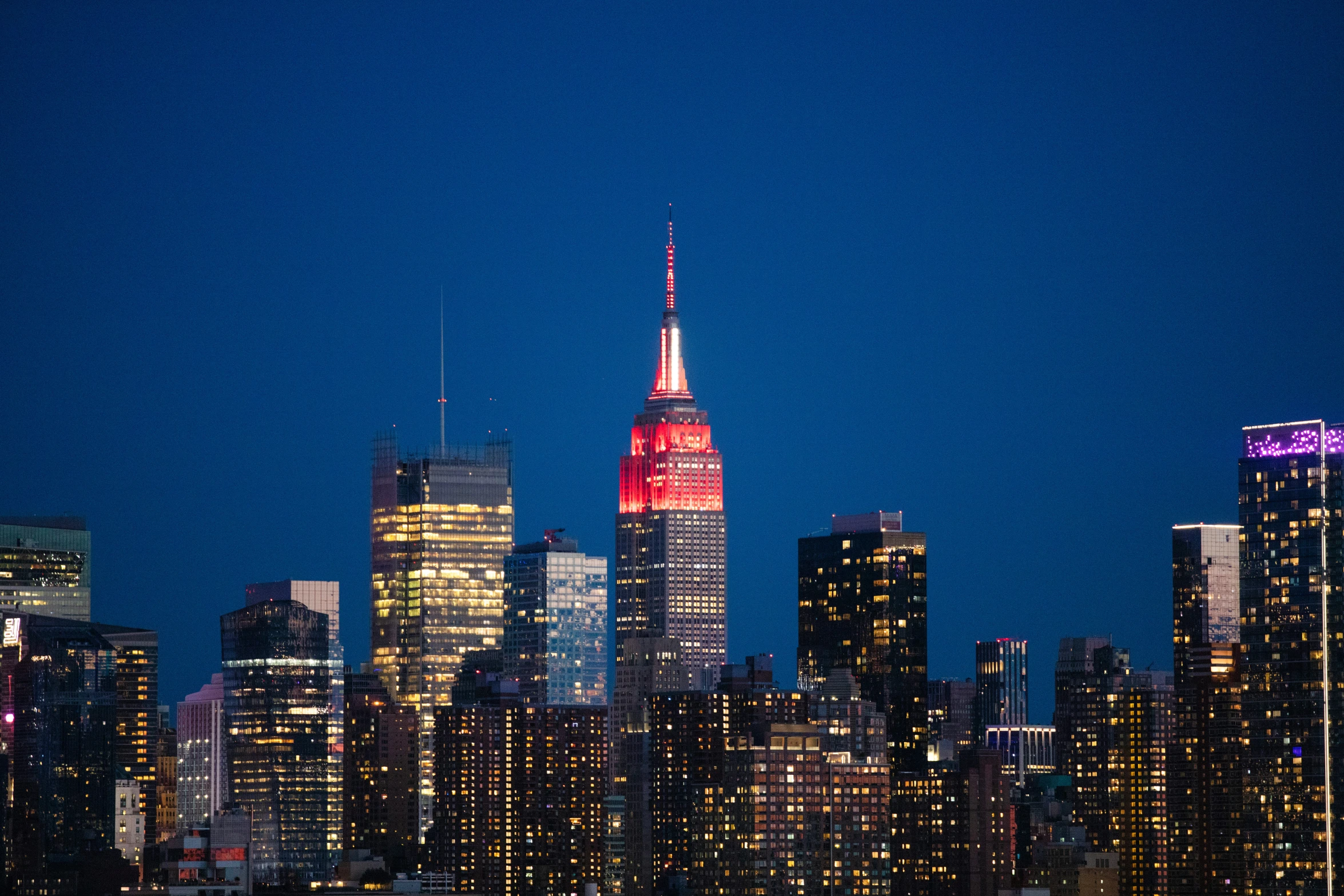 the red lighted spire and surrounding skyscrs is lit up at night