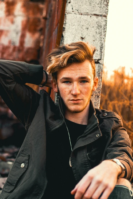 young man sitting down in front of a rusty building