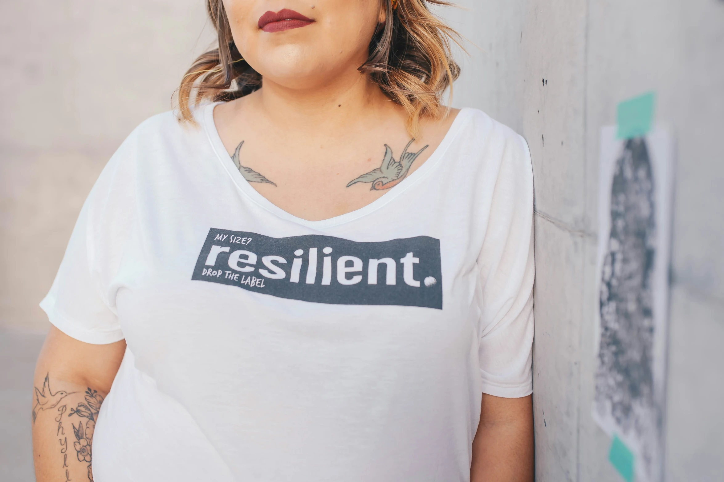 a woman wearing a resilint t - shirt poses by a wall