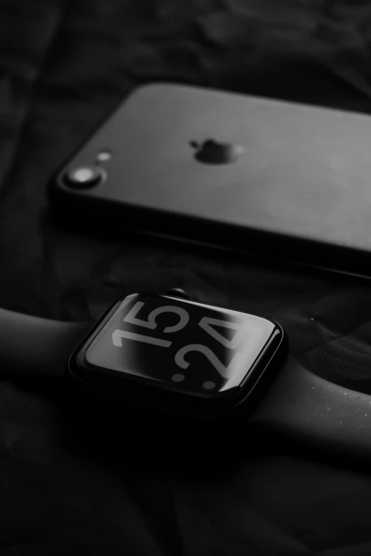 apple watch sitting on a black surface with its battery back and an iphone showing