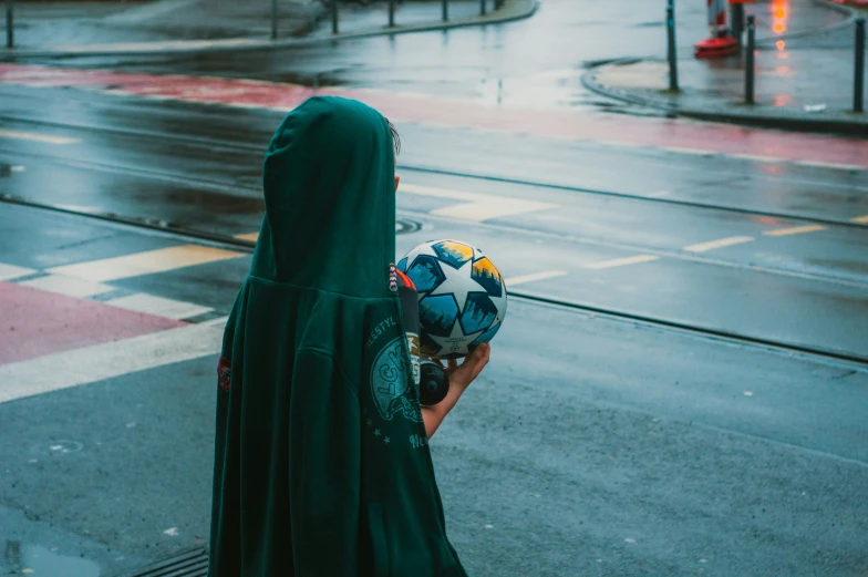 a woman in a green robe holds a hat and looks at the street