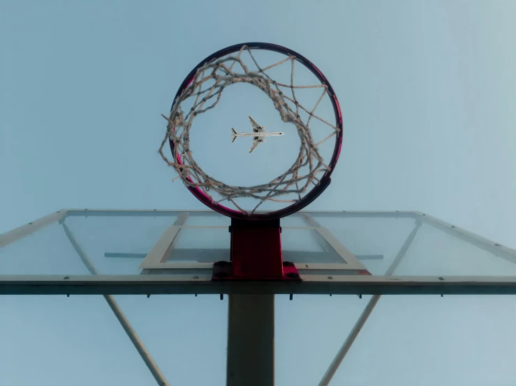 a glass basketball hoop with an airplane flying in the sky