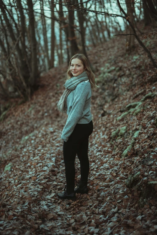 a woman standing on a leaf covered path in the woods