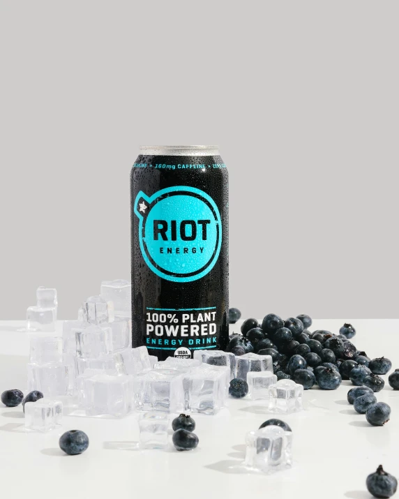 an ice cube and frozen blueberries are seen in front of a black soda can