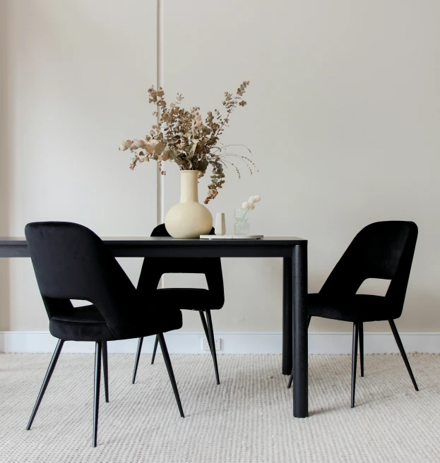 a vase with flowers and black chairs with white walls