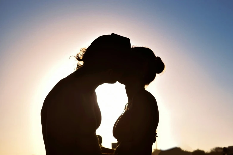 a person kissing another person in silhouette against the sun