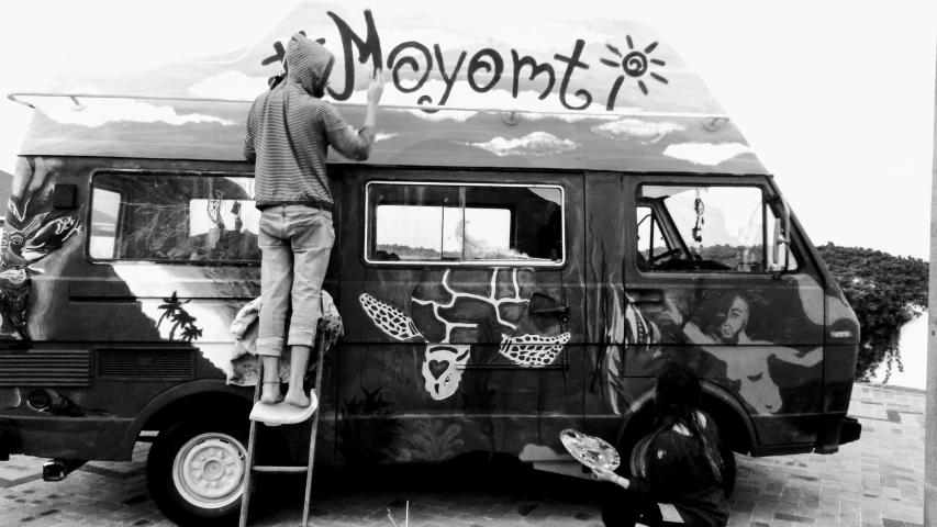 man standing on ladder above a moving van with writing on it