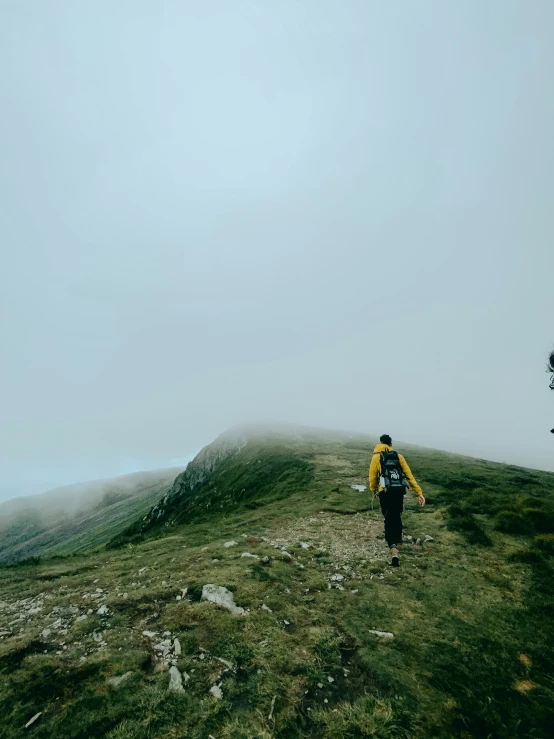 a man in yellow jacket walking across a grassy hill