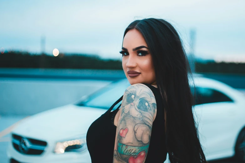 the woman with a black tank top stands in front of a white car