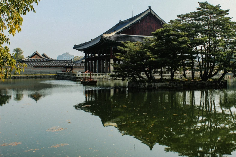 a building with trees in the foreground is surrounded by calm waters