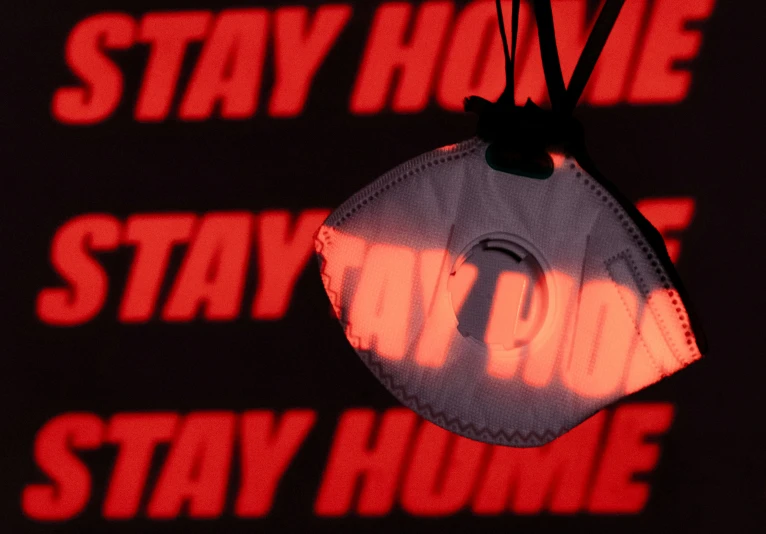 a mask hanging from a hook on a sign saying stay home