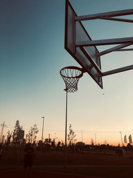 an outdoor basketball court, with a basketball going through the hoop