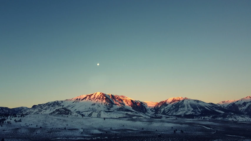 the moon above the snowy mountains, in front of a blue sky