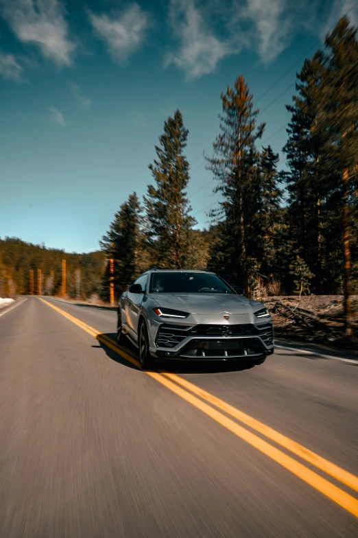 an expensive sports car drives down a street near some pine trees