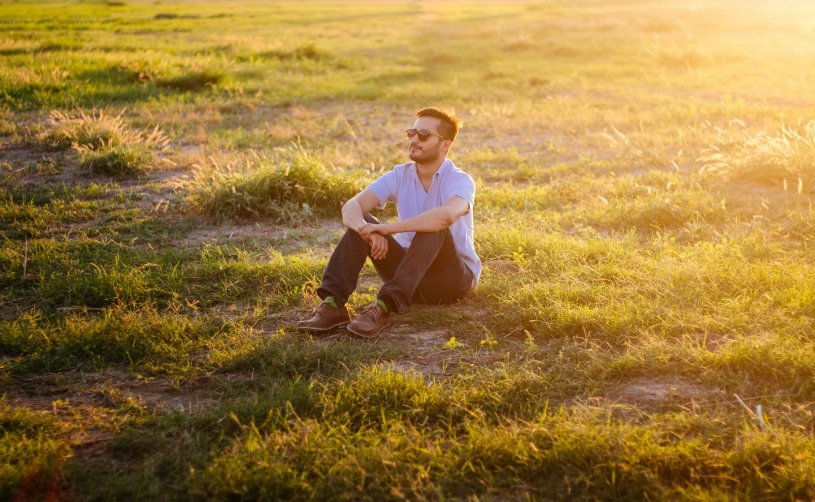 a man in white shirt sitting on ground next to grassy field