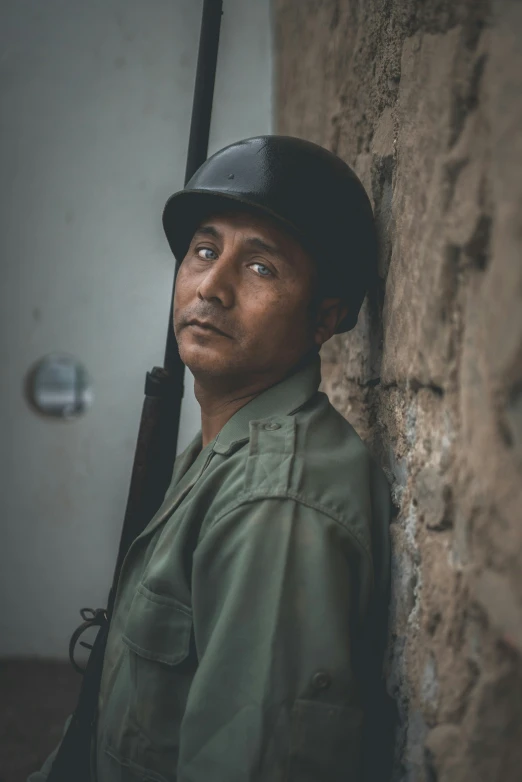 a man leaning on the wall holding a gun