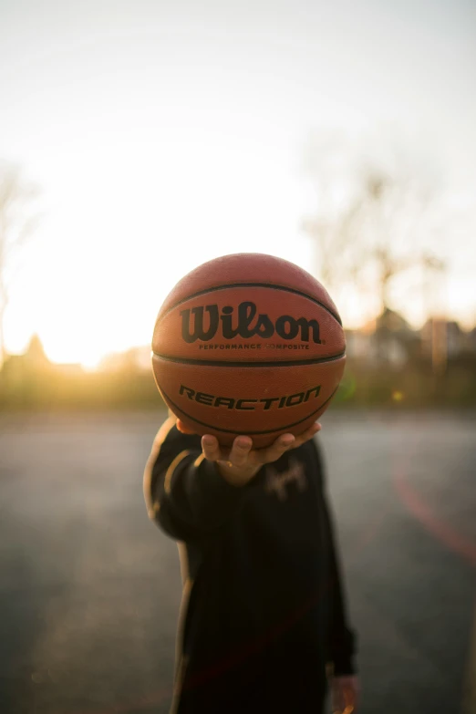 an person is holding up a basketball with the sun in the background