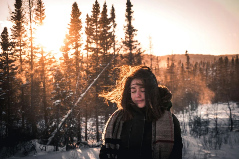 woman standing alone in snowy woods watching the sun set
