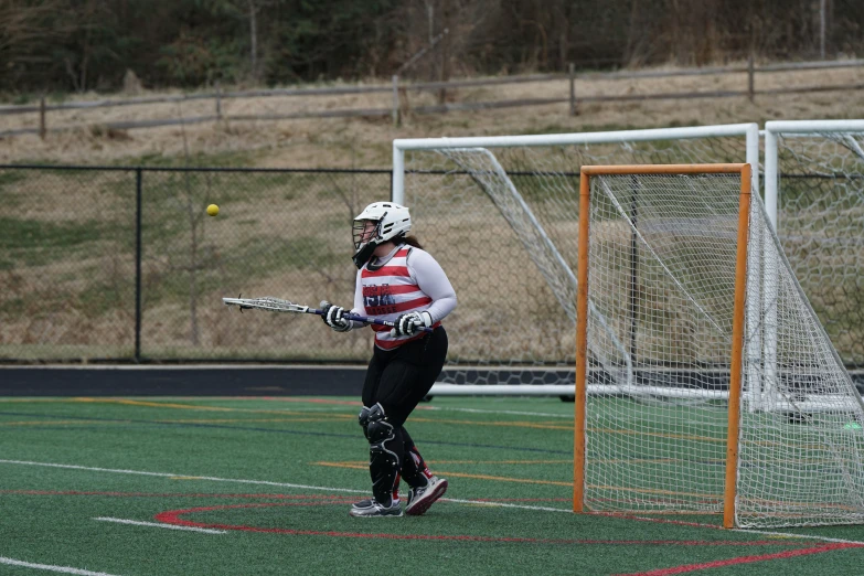 young woman playing lacrosse wearing protective gear and standing on the field