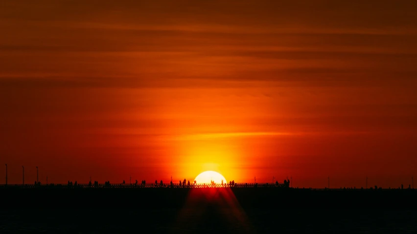 the sun setting behind a lighthouse on the water