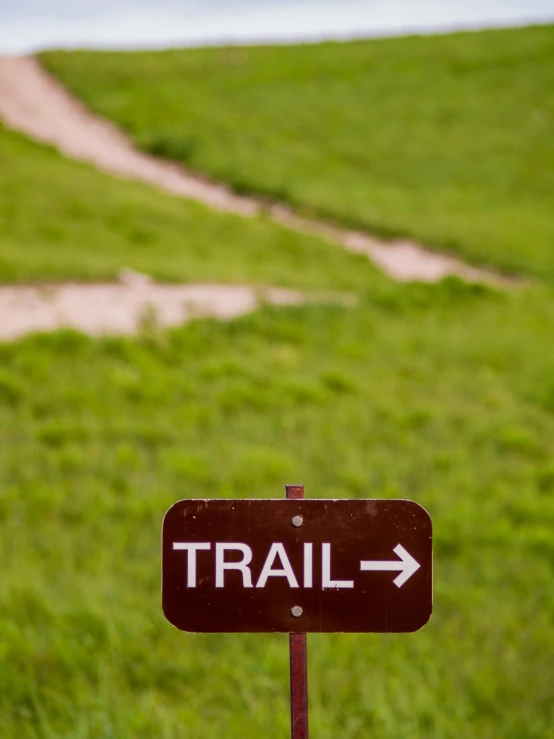 trail uphill with arrow sign on post on grassy hill