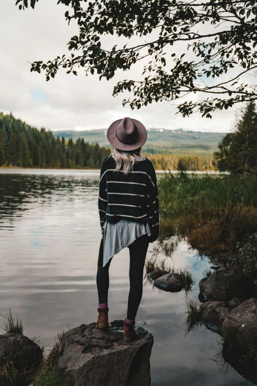 a woman standing on top of a rock near the water