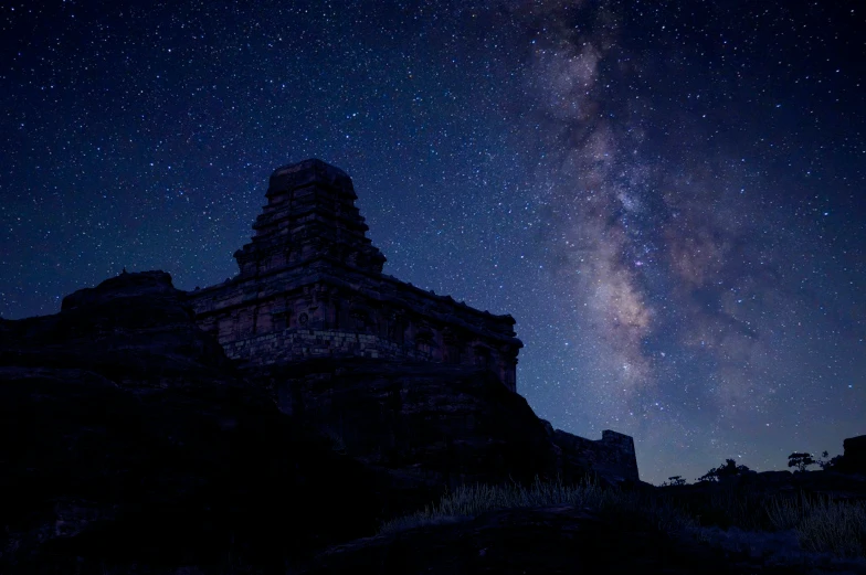 the night sky with stars over a rock tower