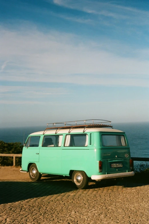 a vw bus sits at the top of a hill near the ocean