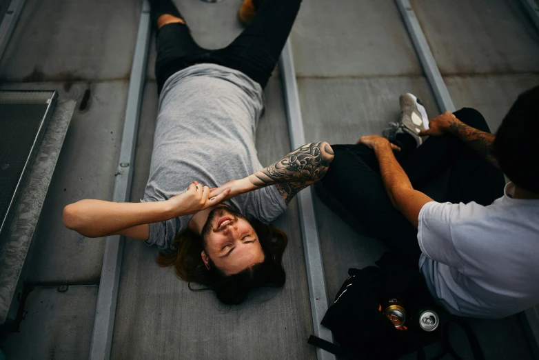 a woman lies on the floor as a man with tattoos on his arm reaches up towards her