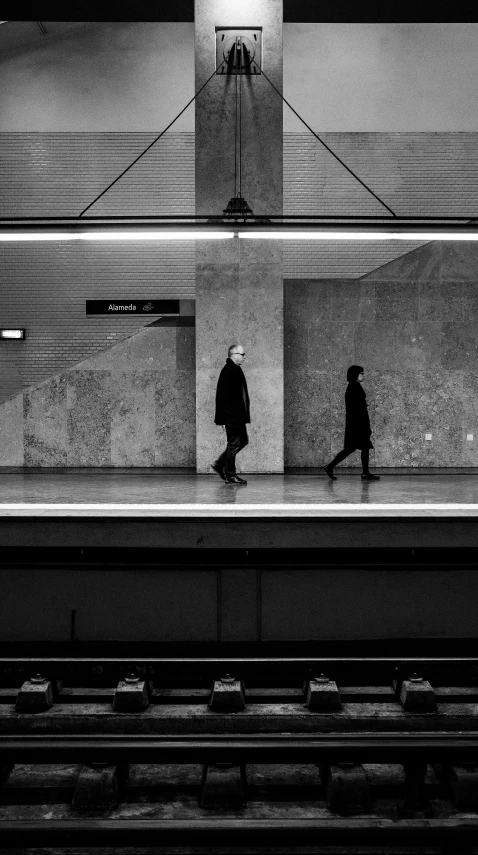 black and white image of two people walking along a train station