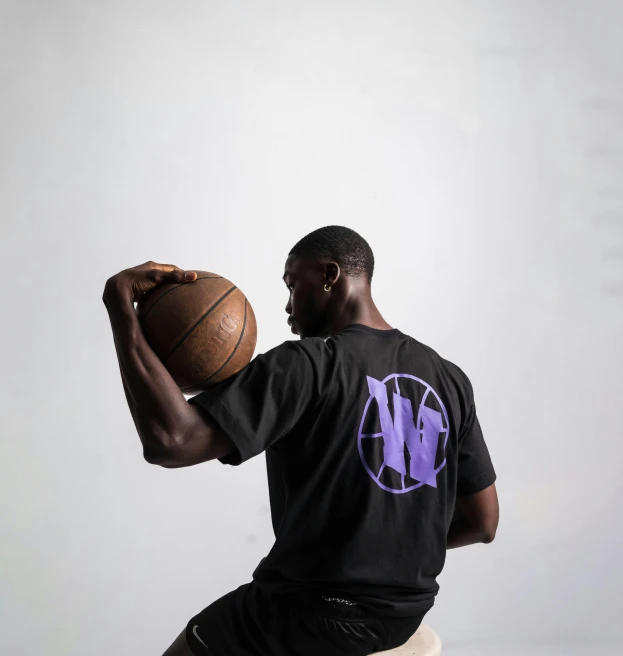a man in black shirt sitting on a white stool holding a basketball