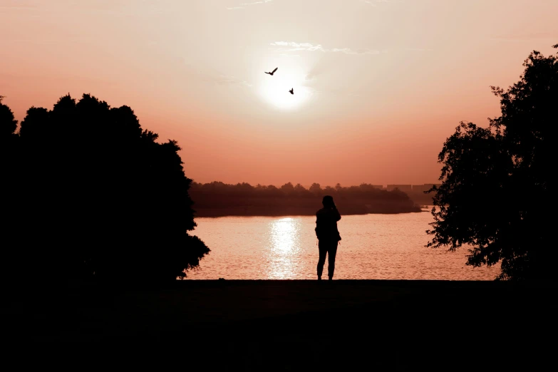 the person stands alone at the sunset on a lake
