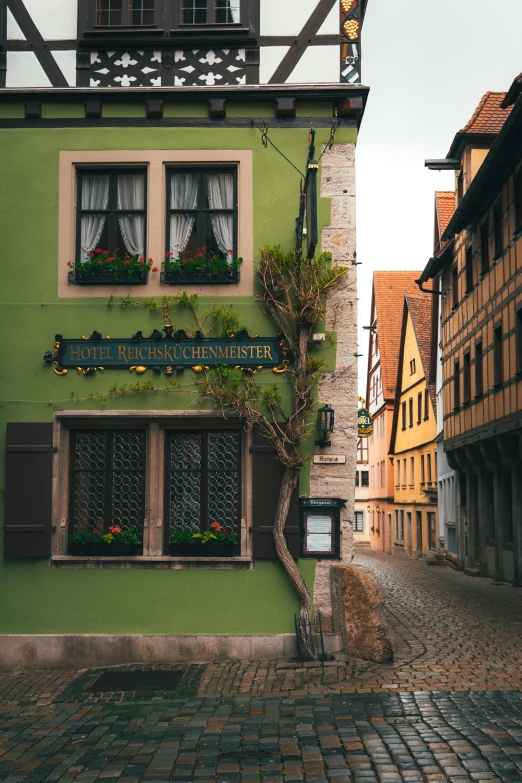 an old green building with two story windows and plants on the balcony