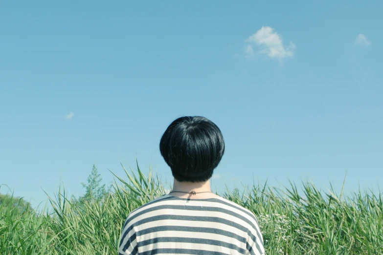 a boy walking away from the camera toward some tall grass