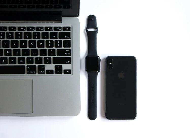 an apple phone, keyboard and accessories next to an open laptop