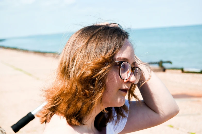 a woman with sunglasses and short red hair stands in front of the ocean on a beach