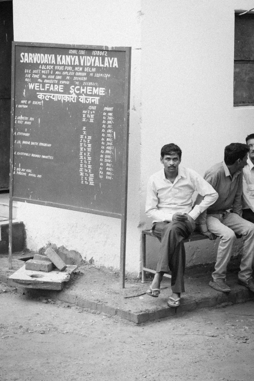 three people are sitting outside beside a sign