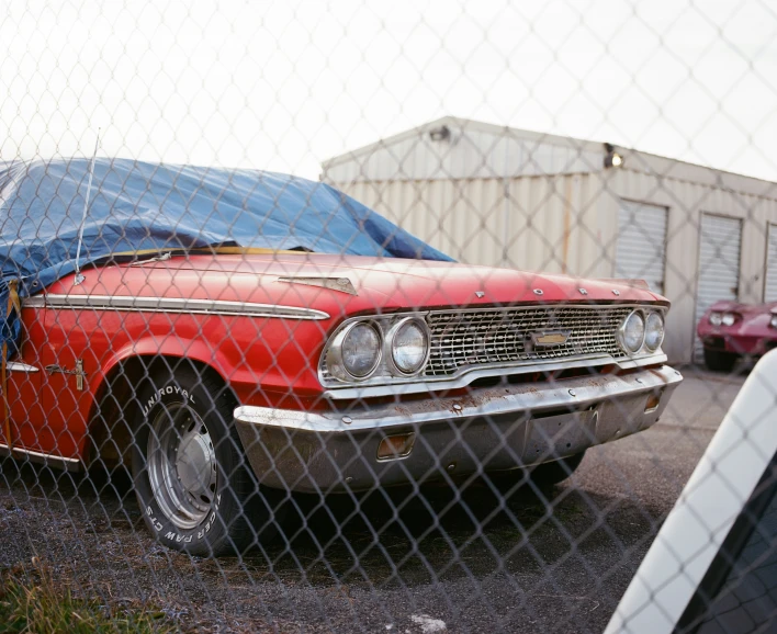 a red car behind a fence with covers on it