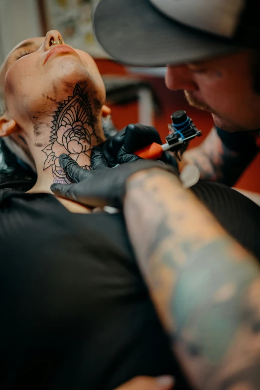 a young woman getting her neck tattooed by an older person