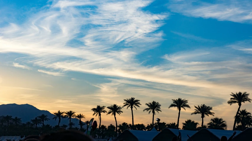 some people are standing under some clouds at sunset